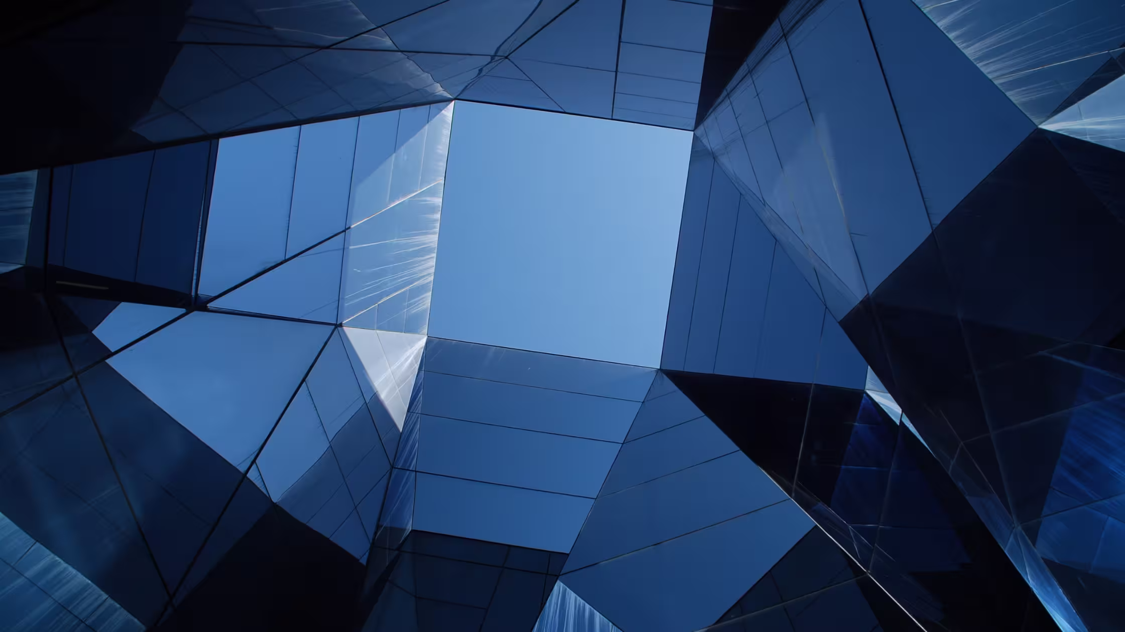 Modern glass building architecture with geometric blue panels forming an open square towards the sky